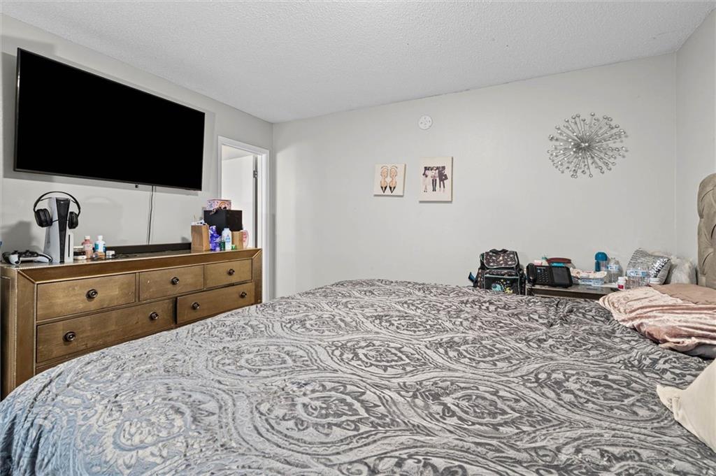 Bedroom with a large patterned bedspread and a wall-mounted television above a wooden dresser.
