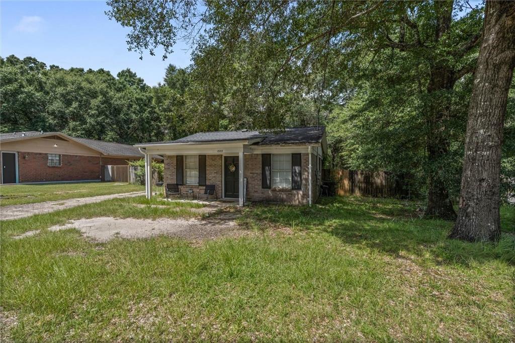 Single-story brick house with a covered porch, grassy yard, and mature trees.