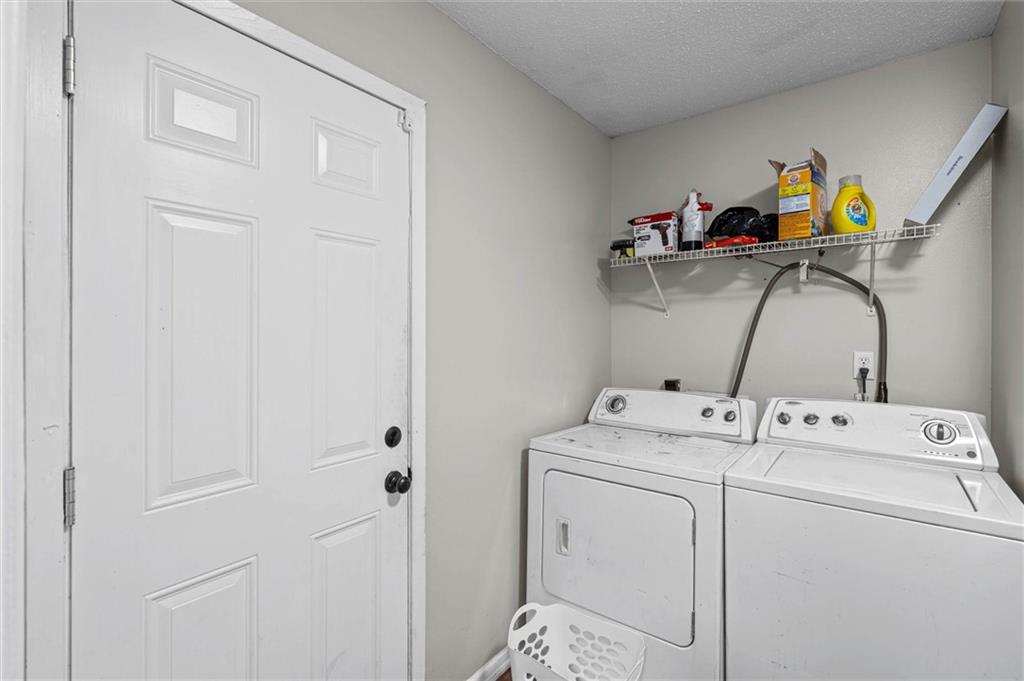 Laundry room with white washer and dryer beneath a wire shelf of supplies.