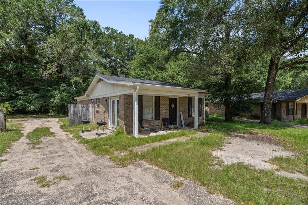 Single-story brick house with a covered porch, gravel driveway, and mature trees.