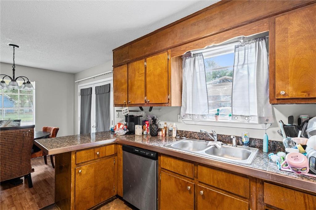 Kitchen with honey-colored cabinets, speckled counters, a double sink, and stainless-steel dishwasher.