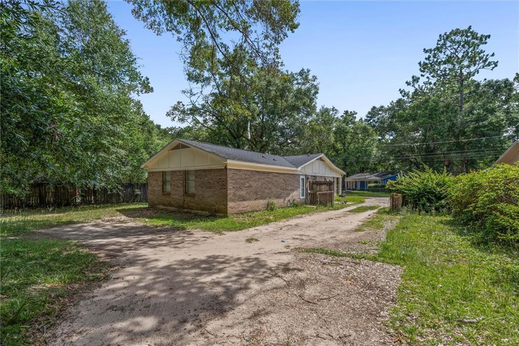 Single-story brick house beside a dirt driveway, surrounded by mature trees.