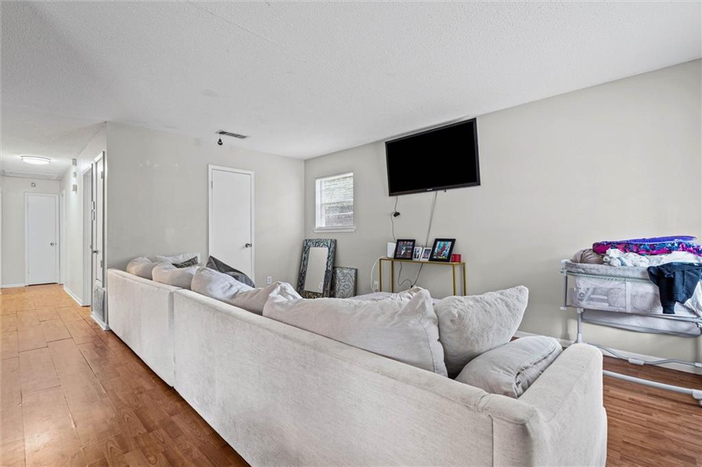 Living room with a cream sectional, wall-mounted TV, wood-look floors, and a bassinet.