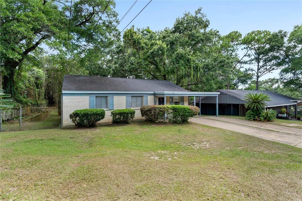 Single-story home with a covered carport, trimmed shrubs, and mature trees around the yard.