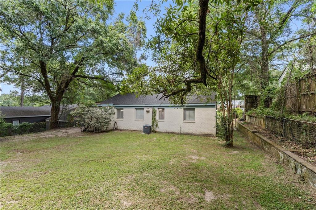 Rear of a single-story brick home beneath mature trees, with a broad grassy yard.