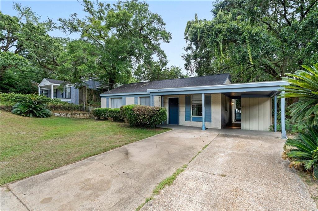 Single-story home with blue shutters, a covered carport, concrete driveway and mature trees.