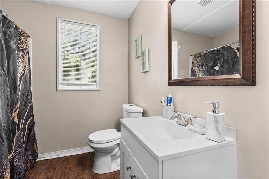 Bathroom with a white vanity, toilet, and dark patterned shower curtain beside a window.
