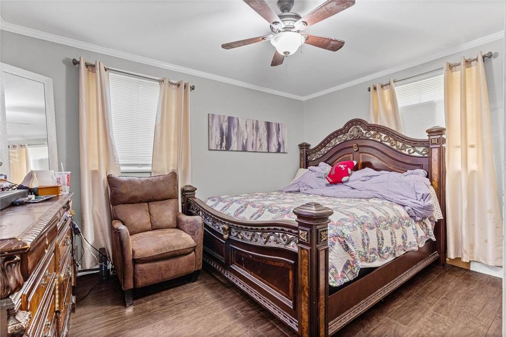 Bedroom with an ornate dark wood bed, patterned quilt, and brown armchair between two curtained windows.