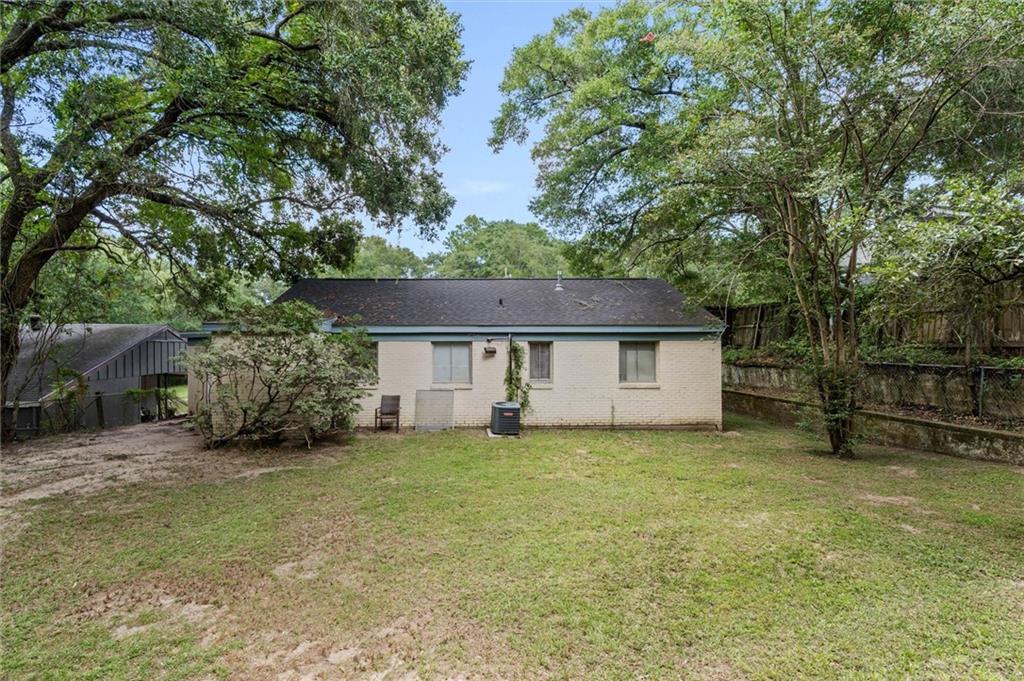 Rear of a single-story brick house across a grassy backyard shaded by mature trees.