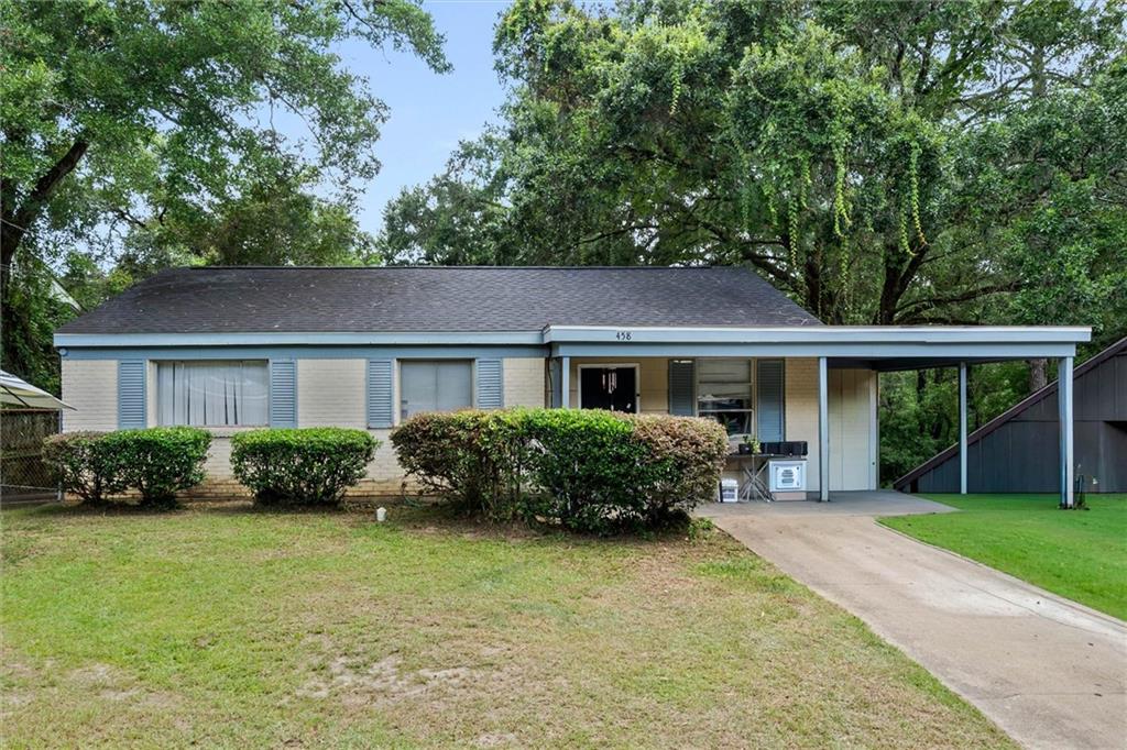 Single-story brick house with blue shutters, an attached carport, and mature trees.