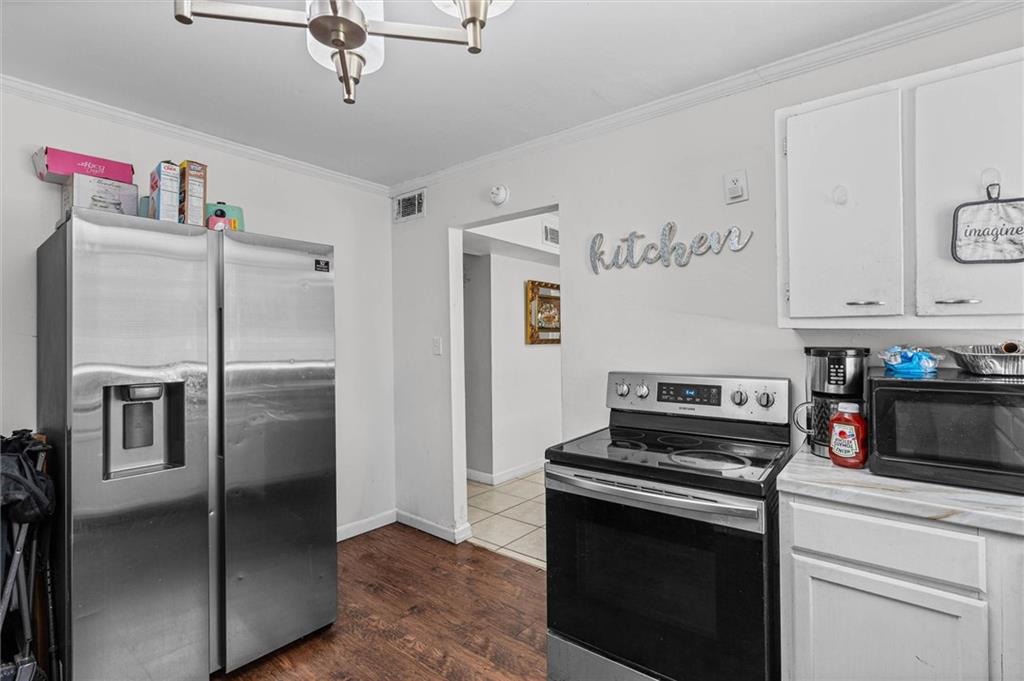 Kitchen with stainless steel refrigerator, black electric range, white cabinets, and contrasting wood and tile floors.