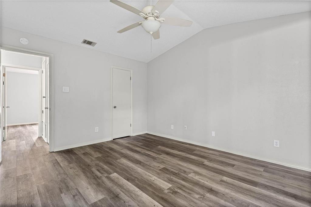 Empty bedroom with a ceiling fan, gray walls, and dark wood-look plank flooring.