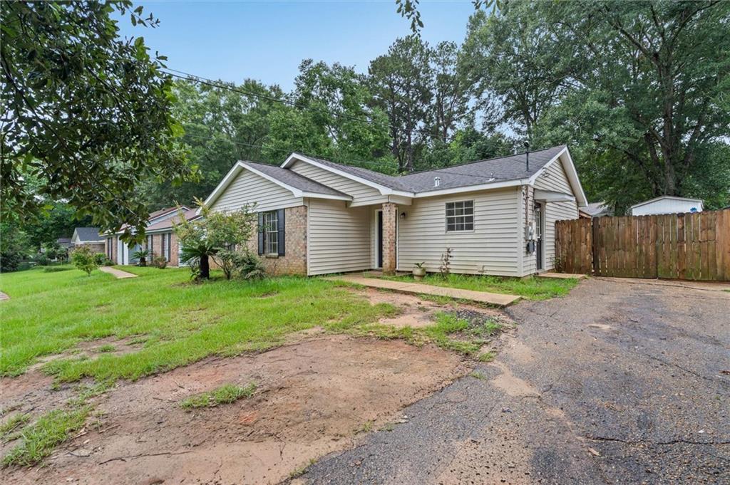 One-story beige house with brick accents, a wooden privacy fence, and a paved driveway.