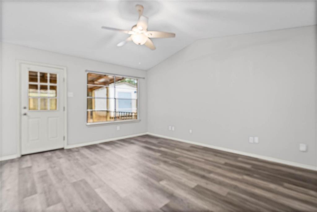Empty room with wood-look flooring, a ceiling fan, and a window beside the exterior door.