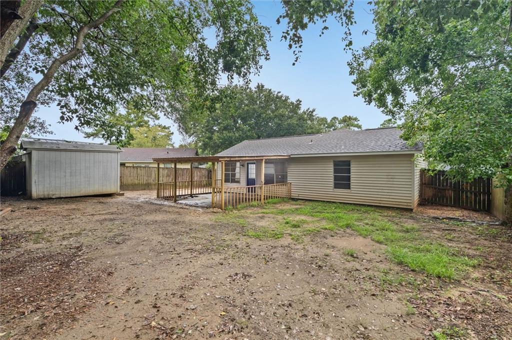 Rear of a single-story house with a small covered deck, detached shed, and spacious tree-shaded backyard.