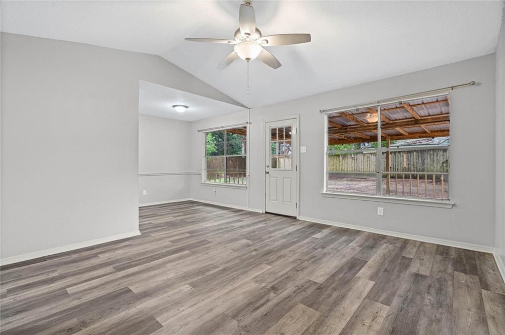 Vacant living room with gray plank flooring, ceiling fan, and windows overlooking a covered patio.