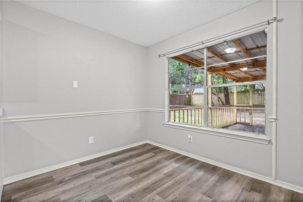 Empty room with gray plank flooring and a large window overlooking a covered wooden patio.