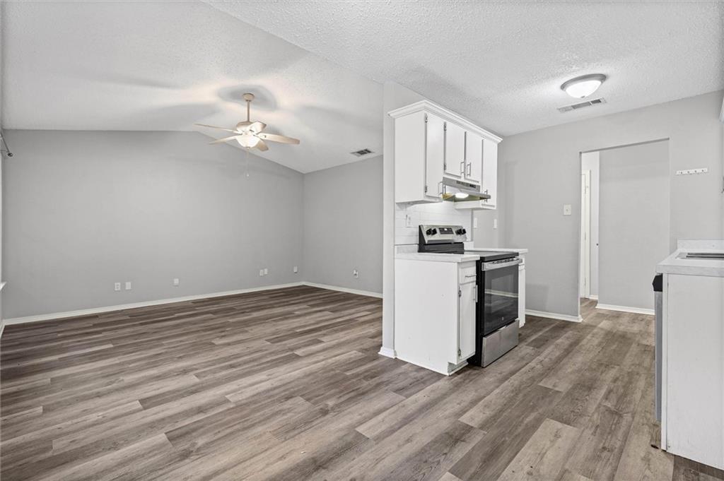 Open-plan living area and kitchen with wood-look flooring, white cabinets, and a stainless steel range.