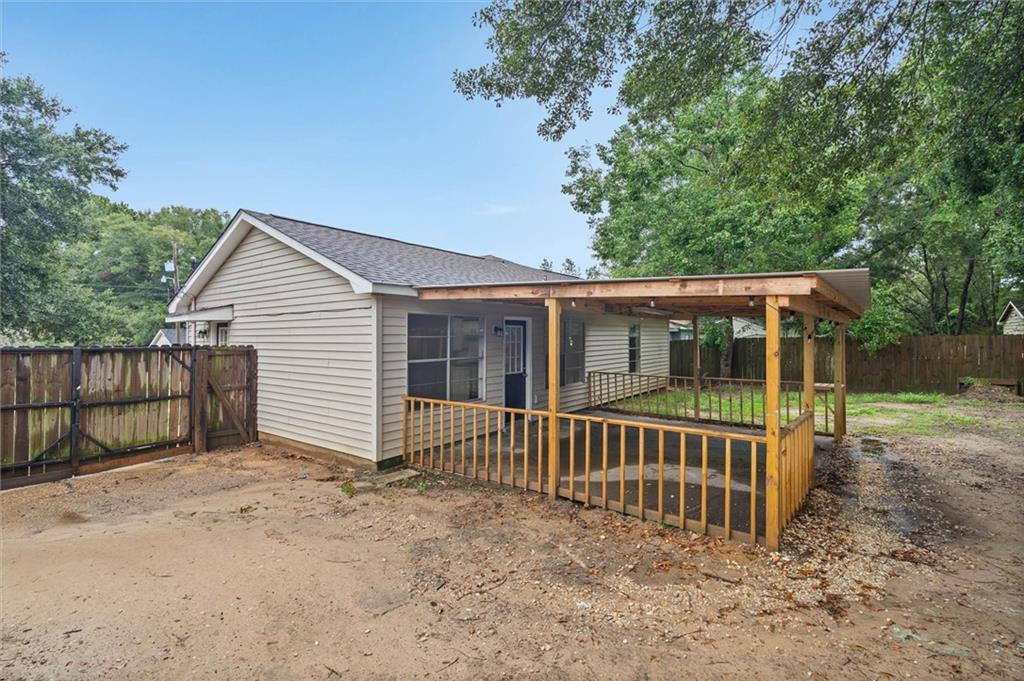 Rear of a light-sided house with a covered, railed patio and fenced backyard.