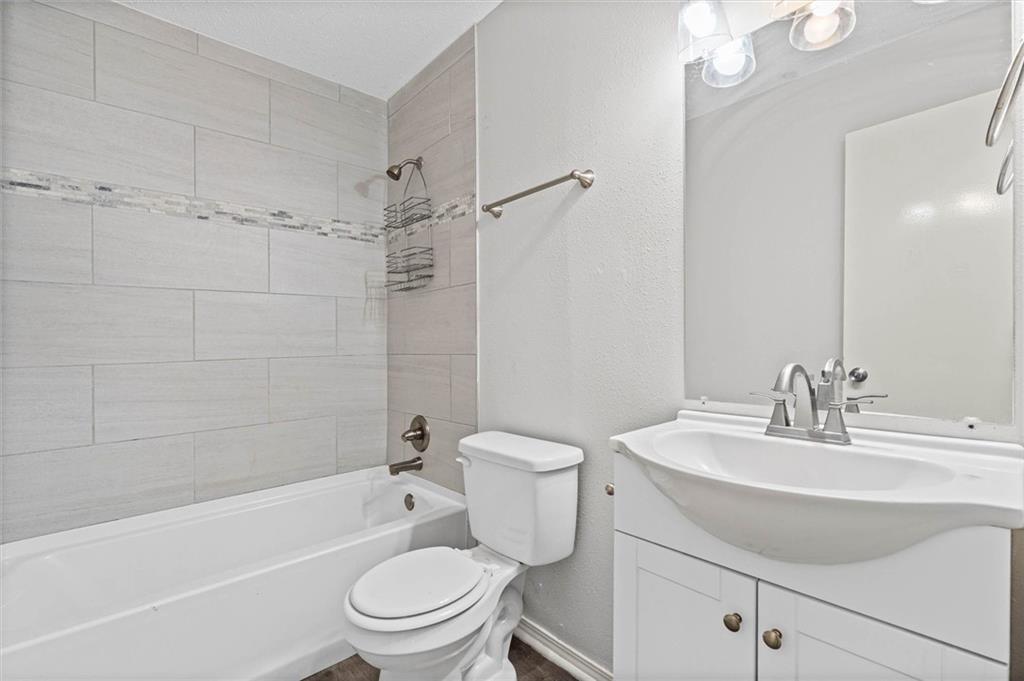 Bathroom with a tiled tub and shower, white toilet, and vanity with an oval sink.