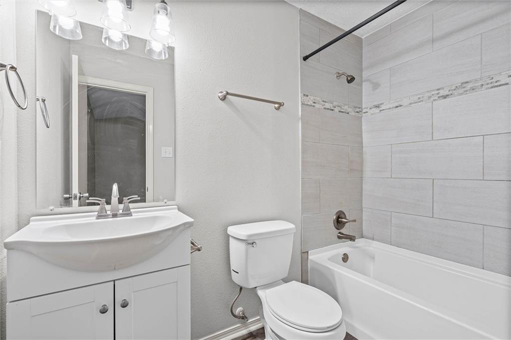 Bathroom with a white vanity, toilet, and bathtub surrounded by large gray tiles.