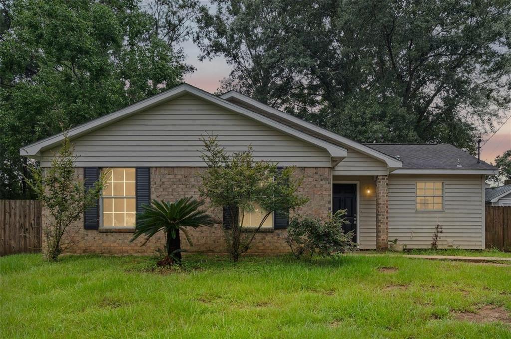 Single-story brick-and-siding home with a broad gabled roof and illuminated windows at dusk.