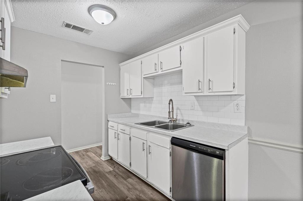 Kitchen with white shaker cabinets, subway tile backsplash, double-basin sink, and stainless steel dishwasher.