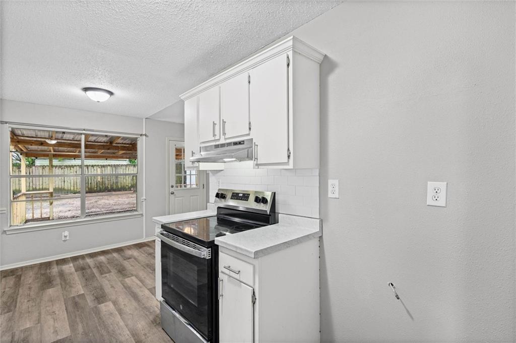 Vacant kitchen with white cabinets, a black electric range, and a window overlooking a covered patio.