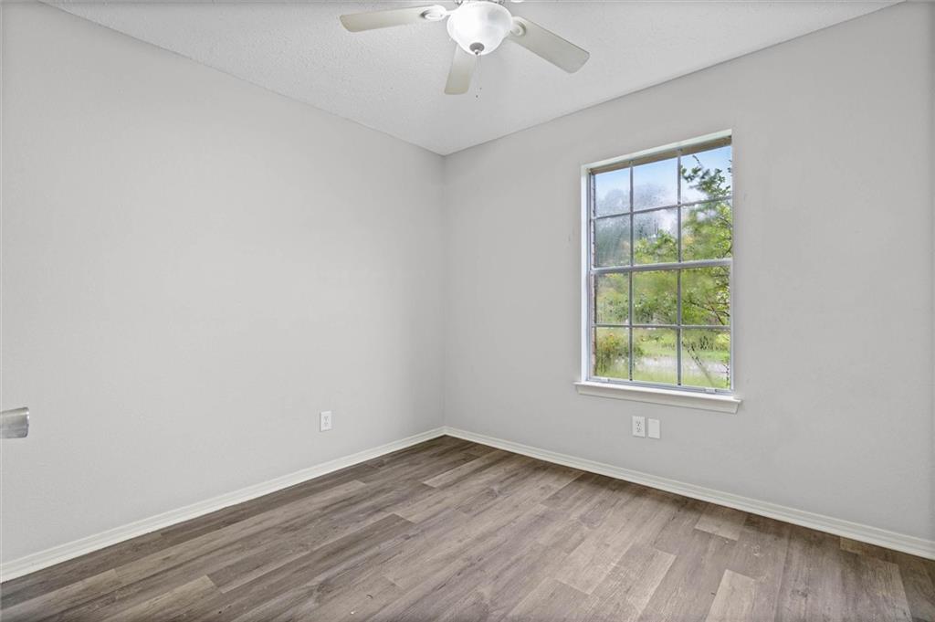 Empty bedroom with wood-look floors, a ceiling fan, and a window facing greenery.