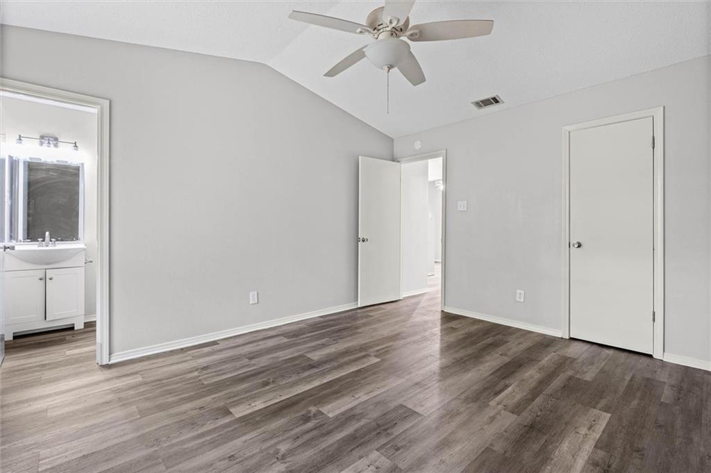 Empty bedroom with wood-look floors, a ceiling fan, and a bathroom vanity visible through the doorway.