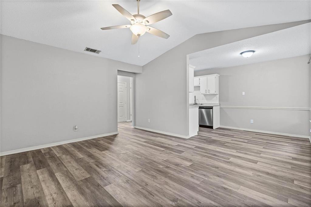 Unfurnished living room with wood-look floors and a ceiling fan, opening to a kitchen.