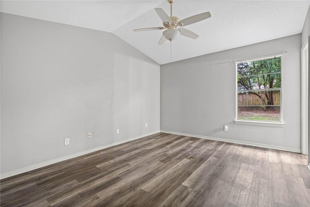 Empty bedroom with wood-look flooring, a ceiling fan, and a window overlooking a fenced yard.