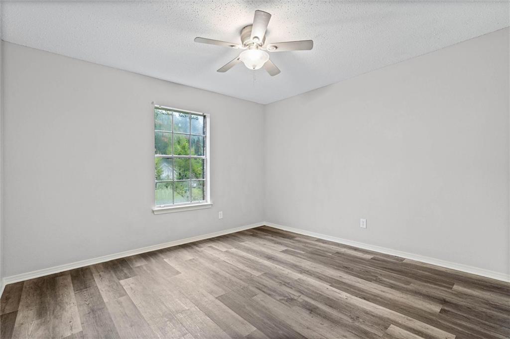 Empty bedroom with gray wood-look flooring, a ceiling fan, and a window overlooking greenery.
