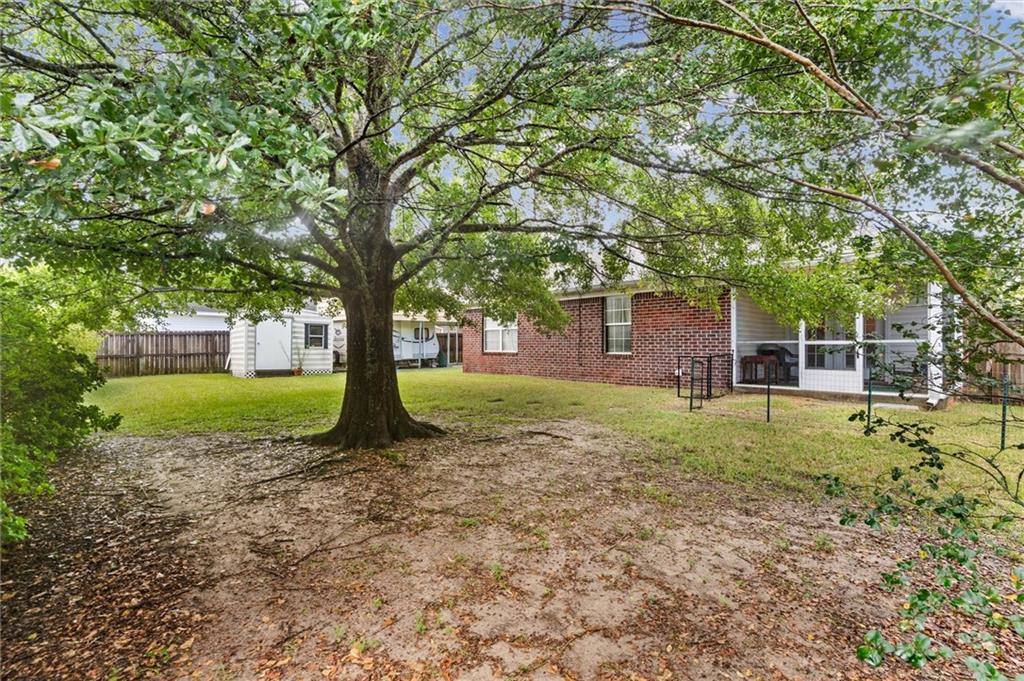 Home’s rear exterior across a shady backyard, with a large tree and covered patio.