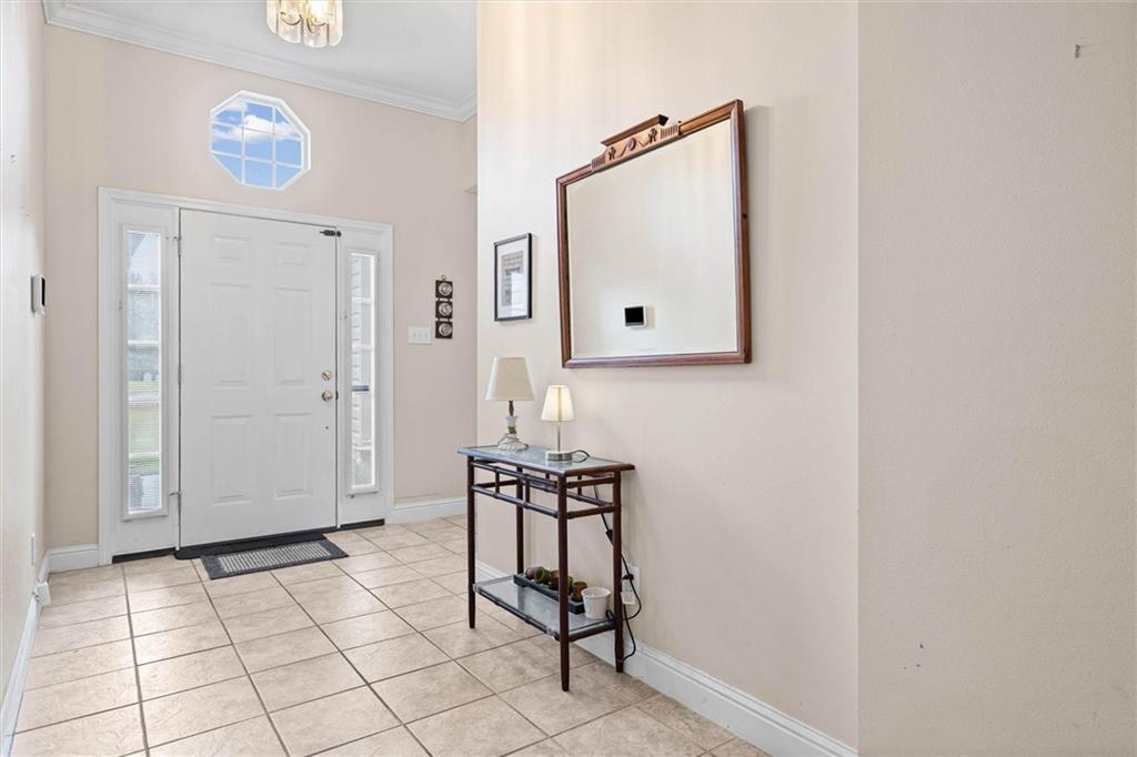 Entry foyer with tiled floors, a white front door, octagonal window, and console table beneath a mirror.
