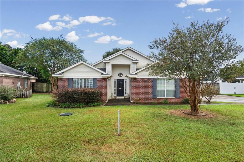 Home with a red brick facade, central black door, broad lawn, and mature trees.