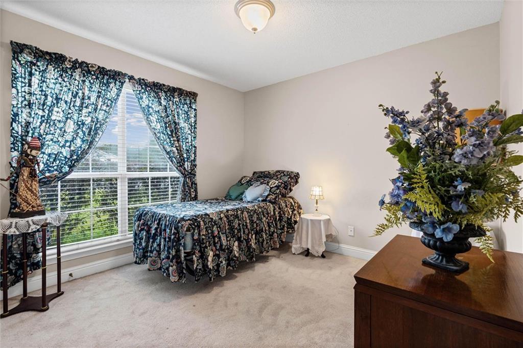 Bedroom with a dark floral bedspread, matching curtains, and a large window with white blinds.
