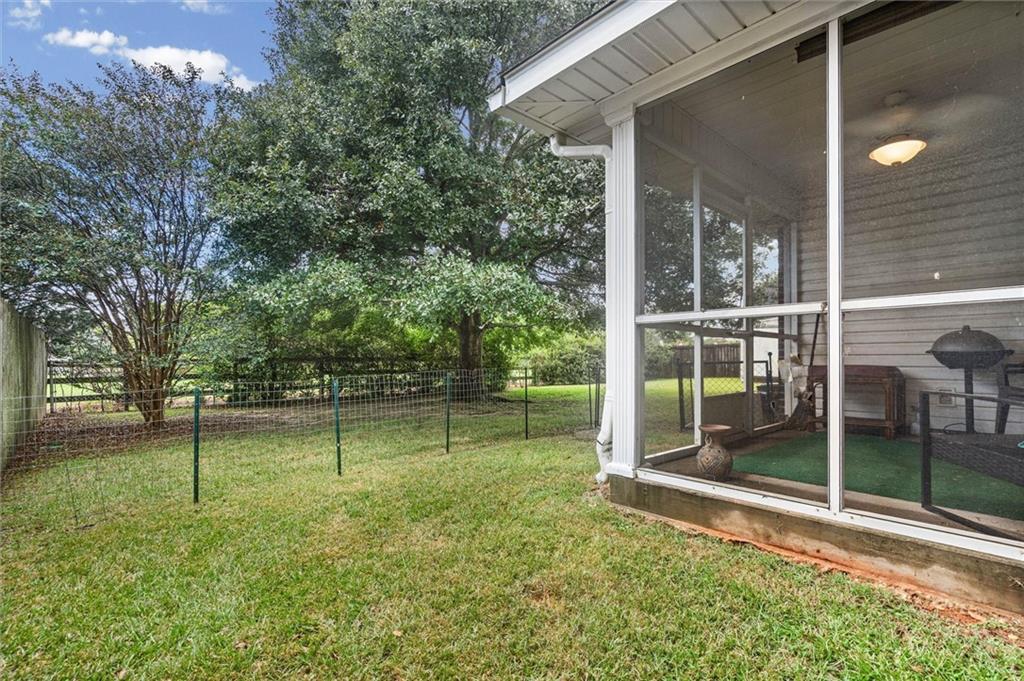 Fenced grassy backyard beside a screened porch, with mature trees and a grill.