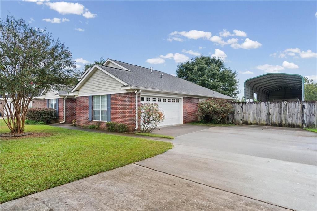 Brick house with an attached garage, broad driveway, and a covered structure behind a wooden fence.