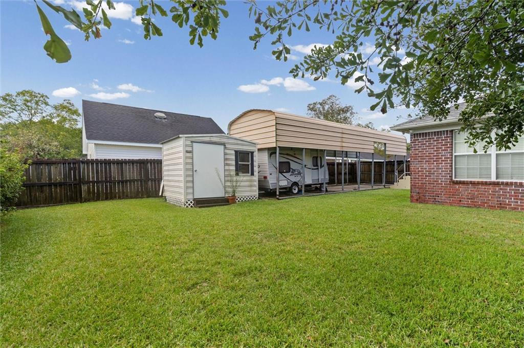 Grassy backyard with a storage shed and covered carport sheltering a recreational vehicle.