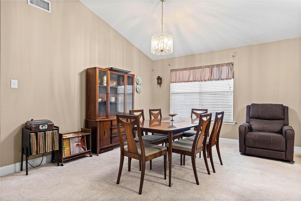 Dining room with a wooden table and chairs, glass-front cabinet, and recliner beneath a vaulted ceiling.