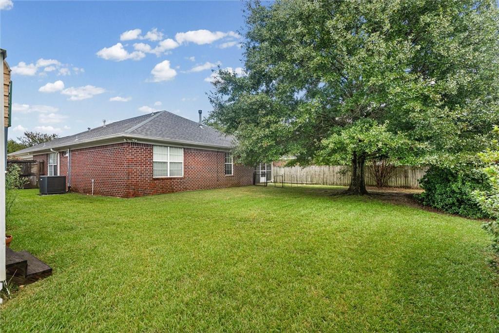 Brick house behind a broad lawn, with a mature shade tree and wooden fence.