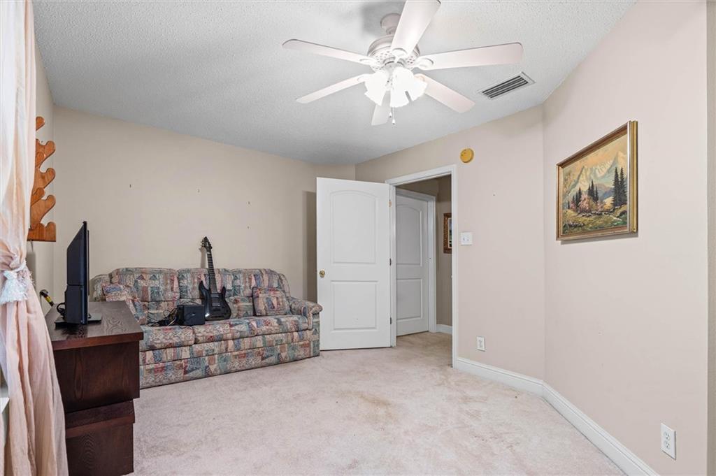 Furnished living room with a patterned sofa, guitar, and ceiling fan.