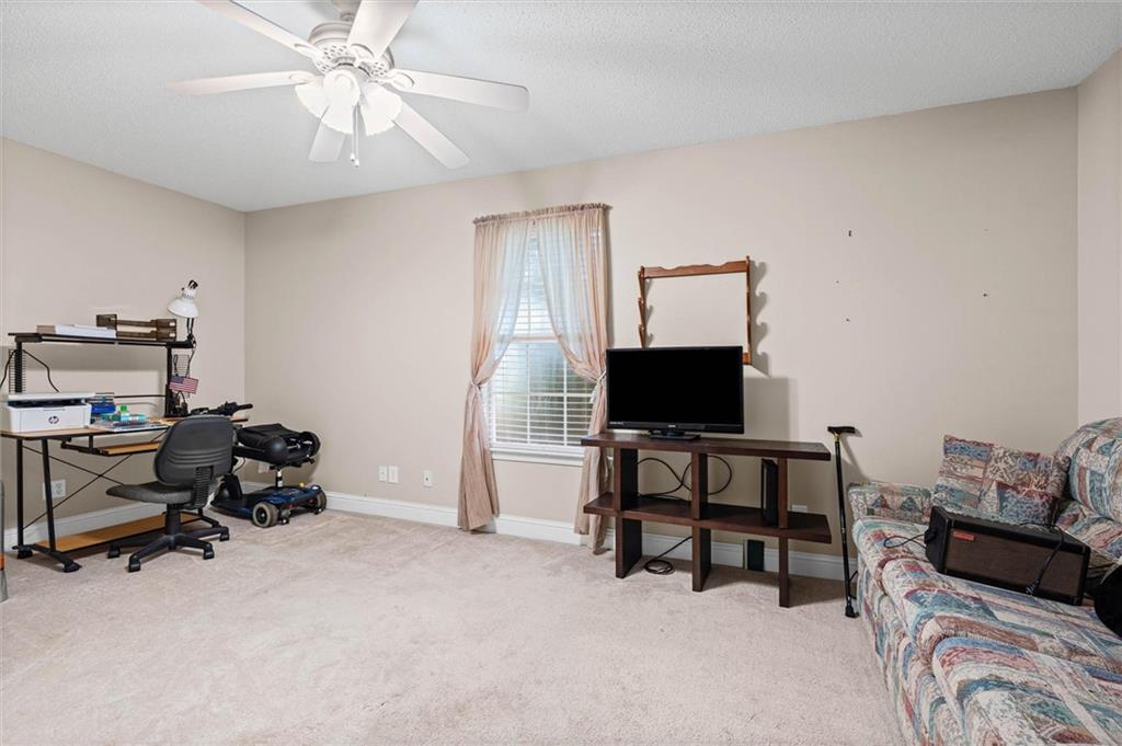 Carpeted bonus room with a desk, television, patterned sofa, and curtained window.