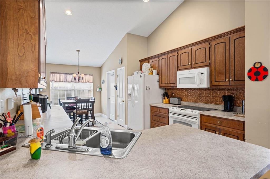 Kitchen with wood cabinets, white appliances, a foreground double sink, and dining area by the window.