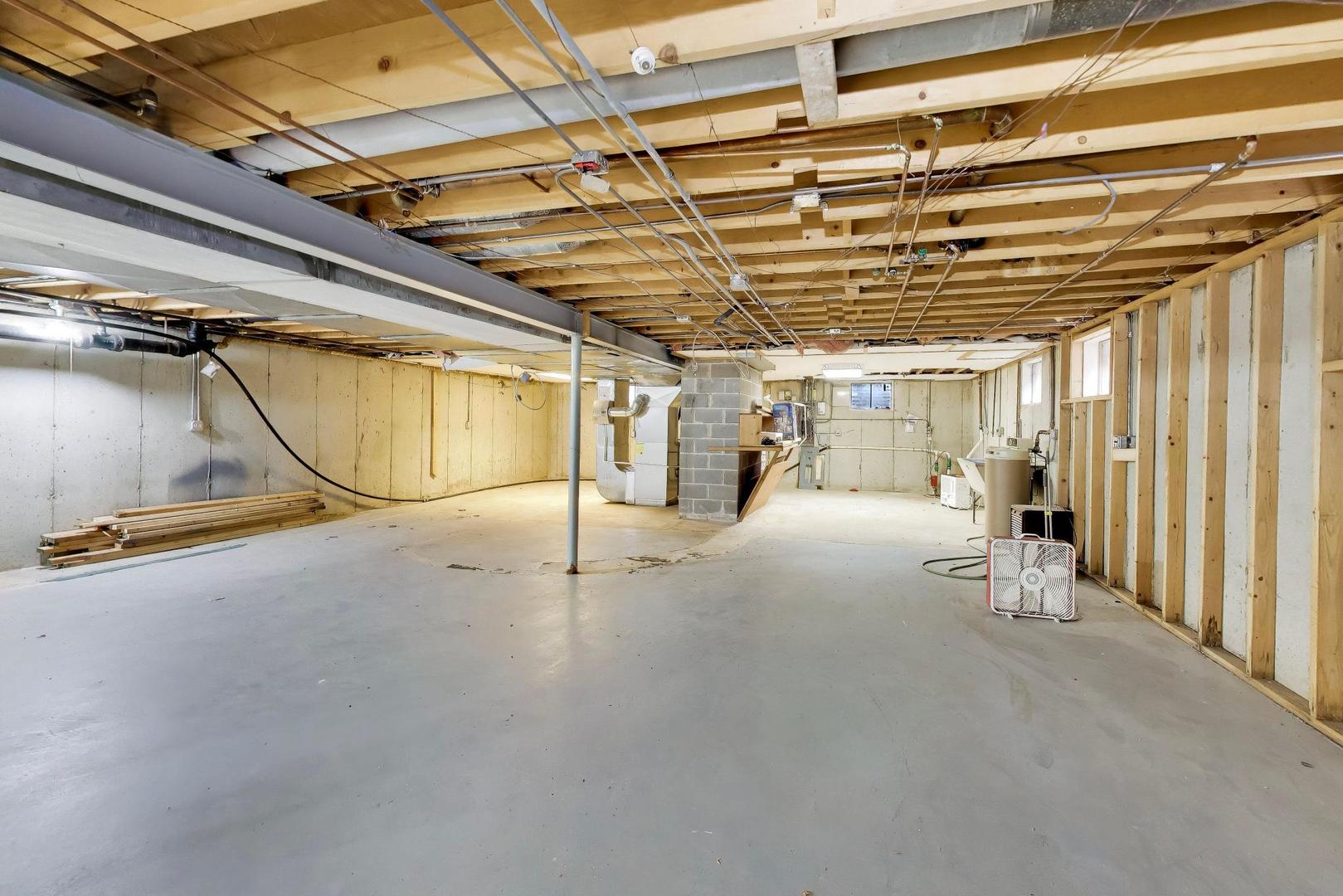 Unfinished basement with exposed ceiling joists, concrete floor, furnace, and open wall framing.