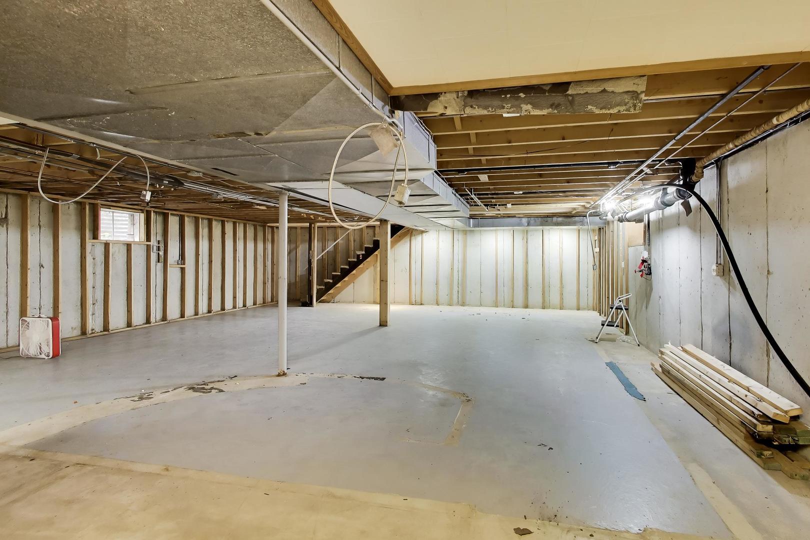 Unfinished basement with exposed framing, ceiling joists, ductwork, and a staircase.