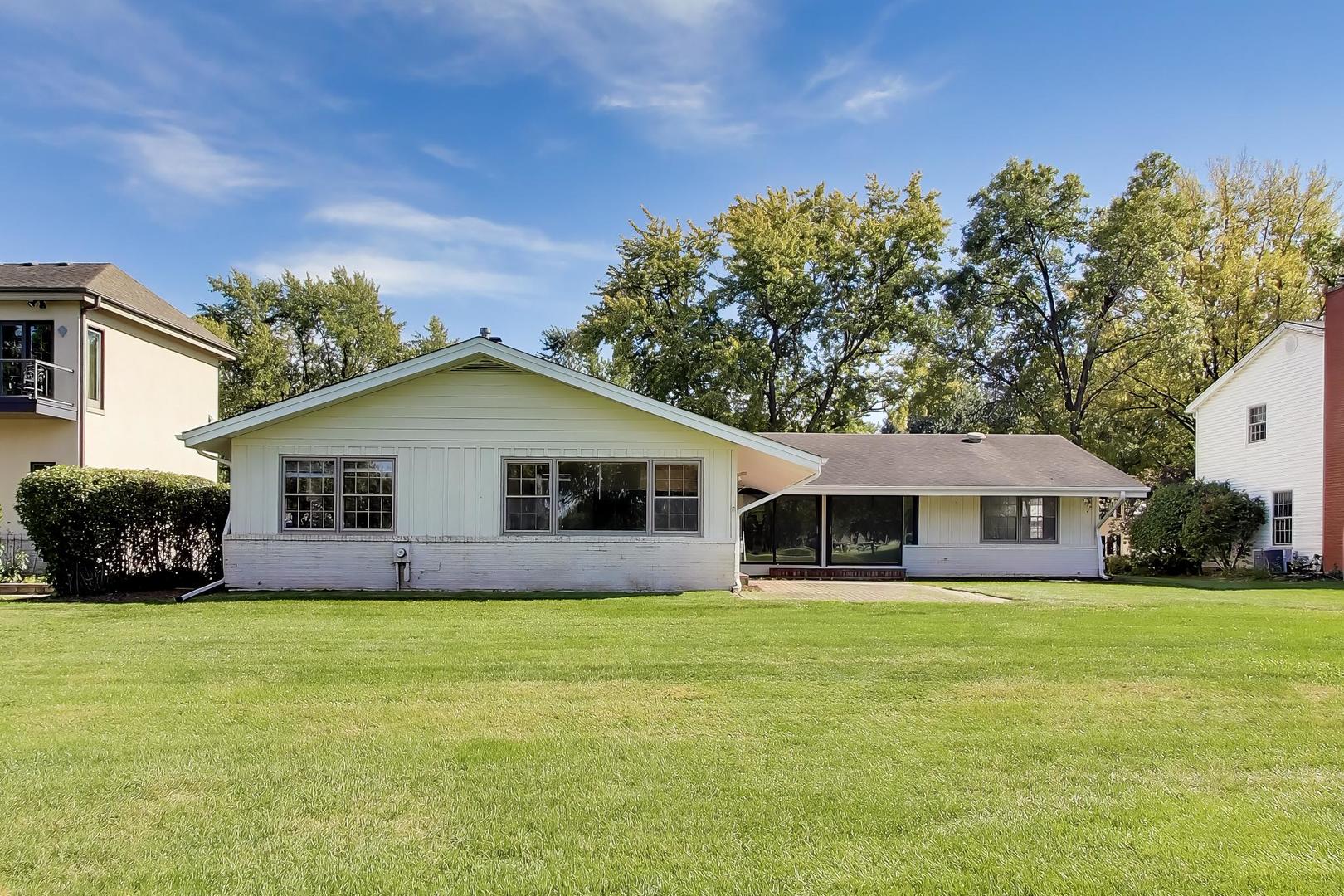 Rear of a single-story white home with large windows, covered patio, and broad lawn.