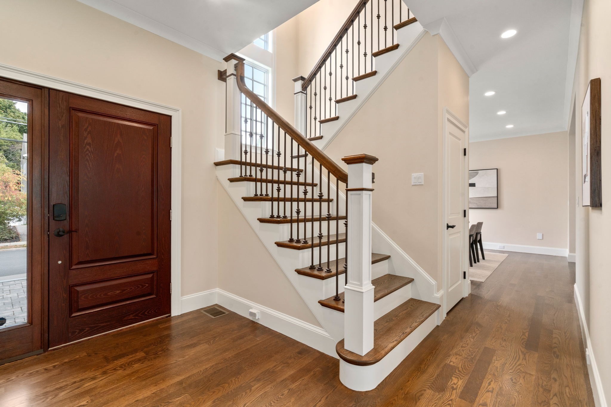Entryway with a dark wood front door and a hardwood staircase with iron balusters.
