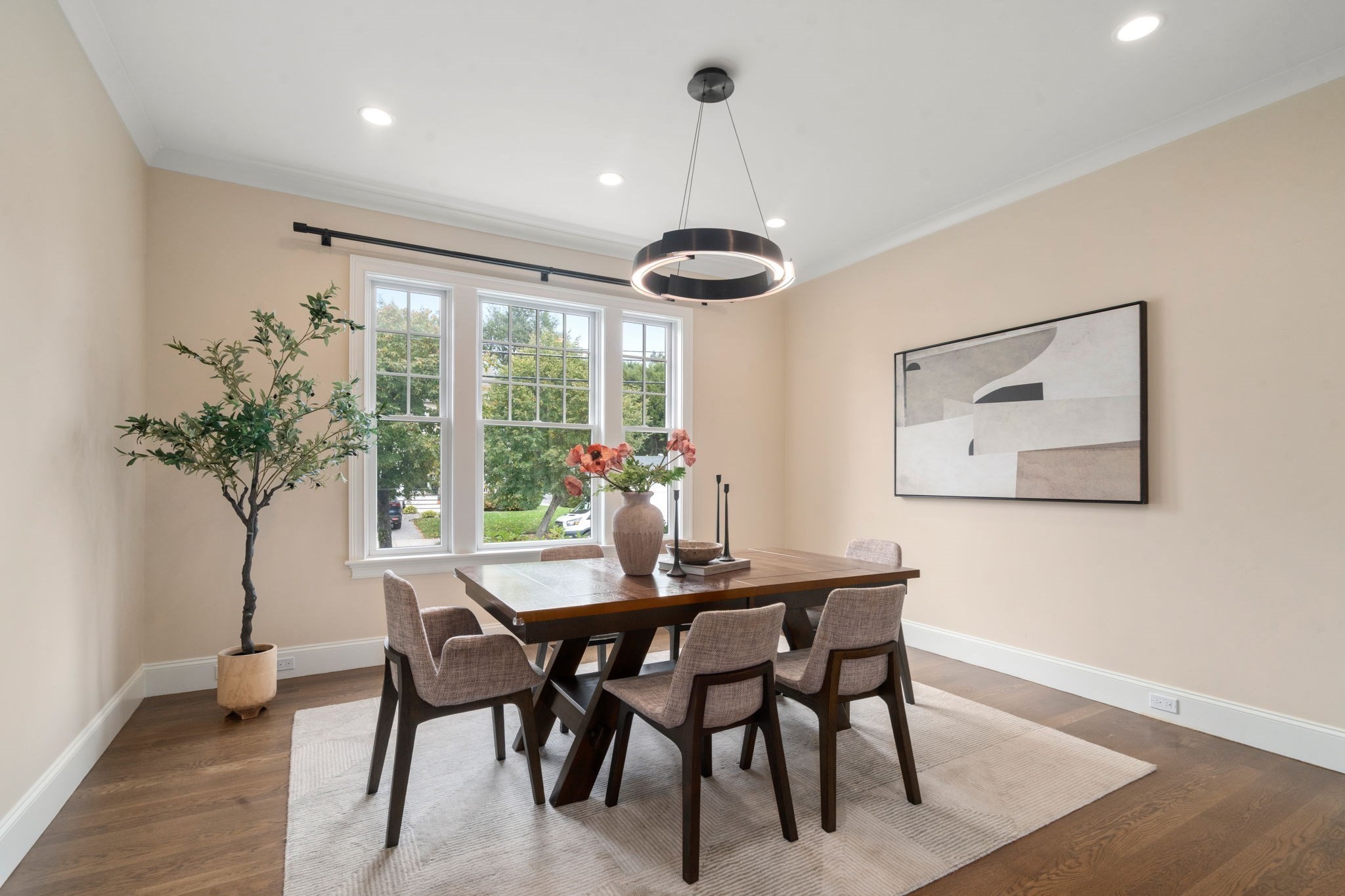 Staged dining room with a dark wood table, upholstered chairs, tall windows, and a circular pendant light.